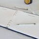 A funeral register book with a blue hardcover open to blank pages with a pen on a table with a white tablecloth.