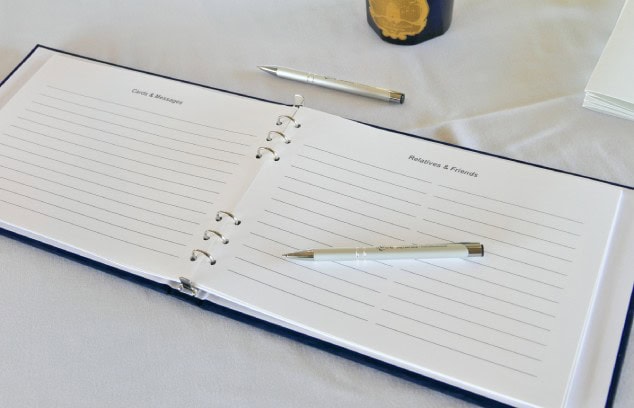 A funeral register book with a blue hardcover open to blank pages with a pen on a table with a white tablecloth.