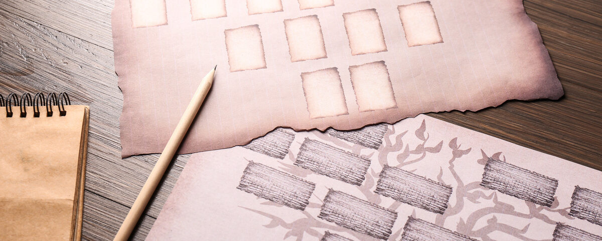 Two pieces of paper with black family tree charts next to a spiral notebook and a pencil on a wooden table.