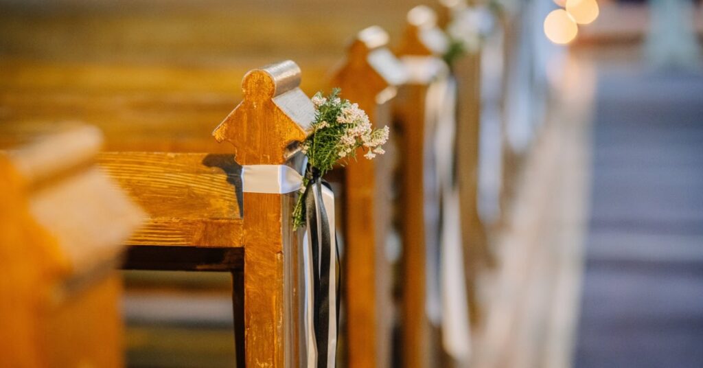 Several wooden church pews have small bunches of flowers tied with white and black ribbons at each end.