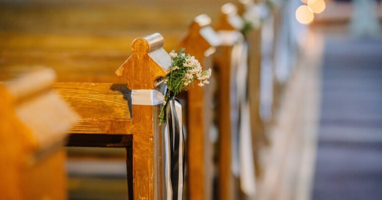 Several wooden church pews have small bunches of flowers tied with white and black ribbons at each end.