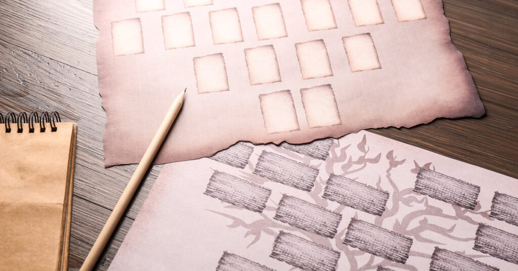 Two pieces of paper with black family tree charts next to a spiral notebook and a pencil on a wooden table.
